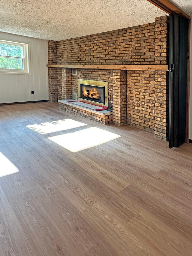21414 Tulip St NW, Oak Grove, MN 55303 - unfurnished living room with wood finished floors, a fireplace, a textured ceiling, and brick wall