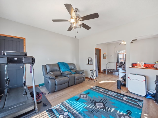 exercise area with wood finished floors, a ceiling fan, arched walkways, and baseboards