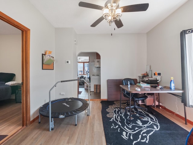 home office featuring wood finished floors, a ceiling fan, arched walkways, and baseboards