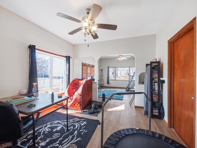 office space with arched walkways, baseboards, ceiling fan, and wood finished floors