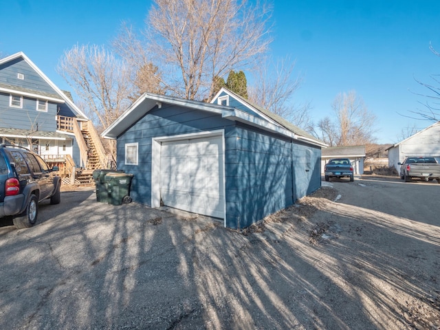 view of outbuilding with aphalt driveway, an outbuilding, and stairs