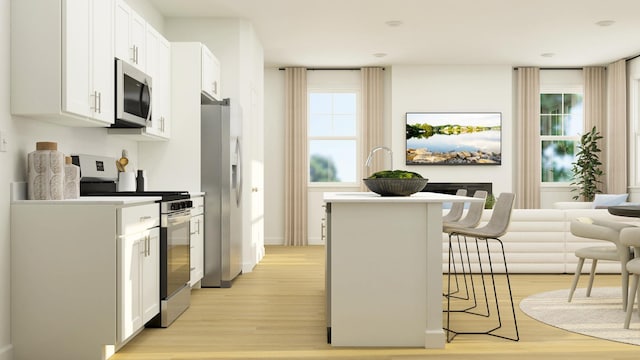 kitchen featuring a kitchen island, a breakfast bar, light wood-type flooring, appliances with stainless steel finishes, and white cabinets