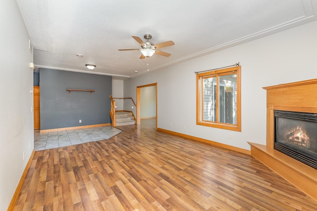 unfurnished living room with stairway, wood finished floors, ceiling fan, and a glass covered fireplace