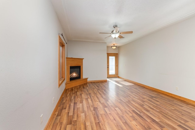 unfurnished living room featuring a glass covered fireplace, light wood-style floors, baseboards, and a ceiling fan