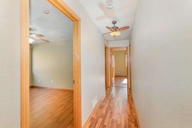 corridor featuring wood finished floors, visible vents, and baseboards