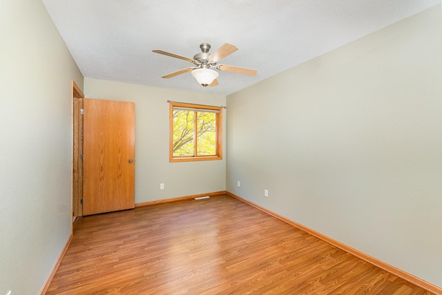 spare room featuring visible vents, ceiling fan, light wood-type flooring, and baseboards