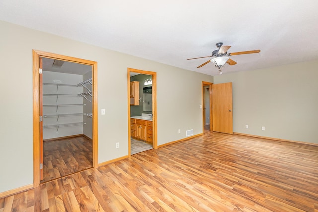 unfurnished bedroom with visible vents, baseboards, ensuite bath, a walk in closet, and light wood-type flooring