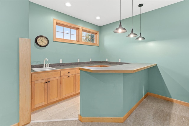 kitchen featuring pendant lighting, a sink, a peninsula, baseboards, and light colored carpet