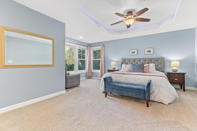 carpeted bedroom featuring a tray ceiling, baseboards, and a ceiling fan