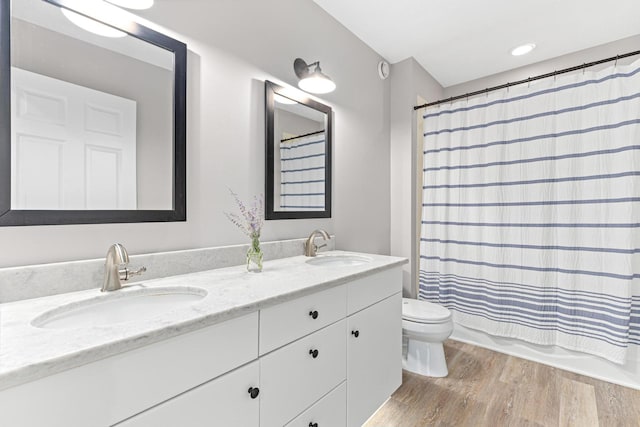 full bathroom with double vanity, wood finished floors, toilet, and a sink