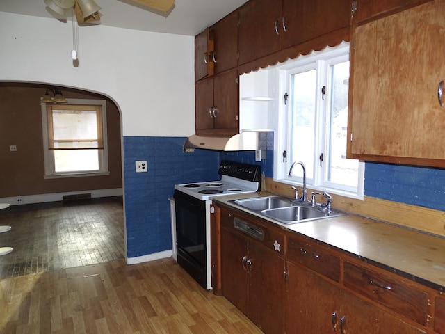 kitchen featuring electric range, light wood-type flooring, a ceiling fan, a sink, and arched walkways