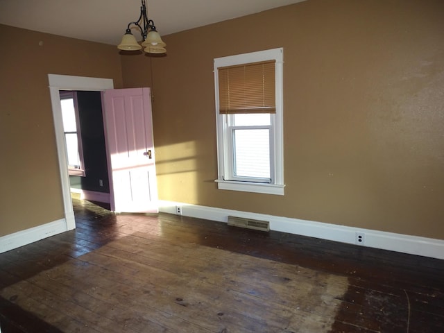 spare room featuring a notable chandelier, dark wood-style floors, visible vents, and baseboards