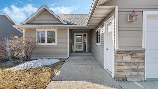 view of exterior entry with a garage, stone siding, and a shingled roof