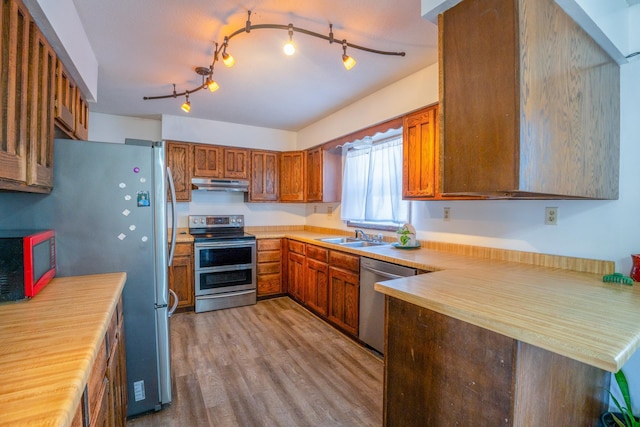 kitchen featuring brown cabinetry, stainless steel appliances, light countertops, light wood-style floors, and under cabinet range hood