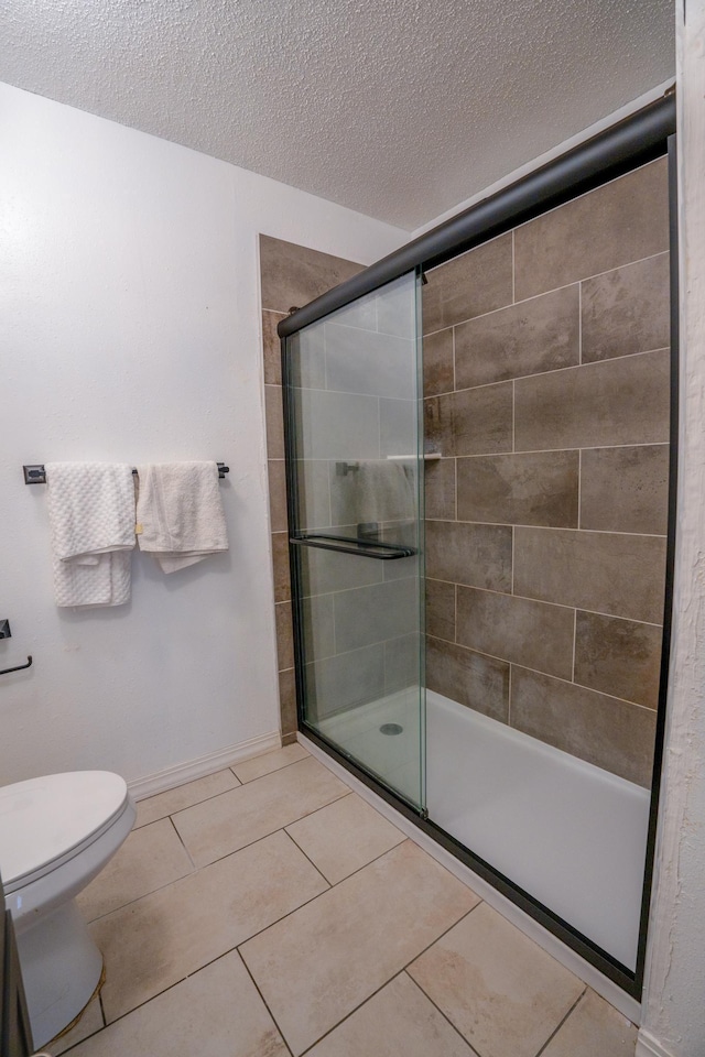 full bath featuring tile patterned flooring, baseboards, toilet, a stall shower, and a textured ceiling