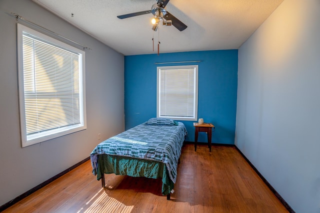 bedroom with baseboards, multiple windows, and wood finished floors