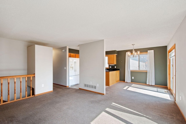 unfurnished living room with baseboards, visible vents, a textured ceiling, light carpet, and a notable chandelier