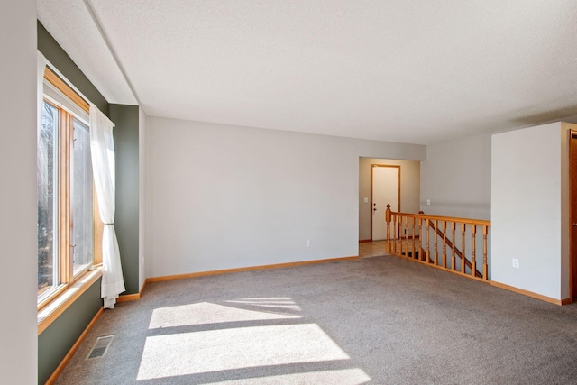 carpeted spare room featuring visible vents, baseboards, and a healthy amount of sunlight