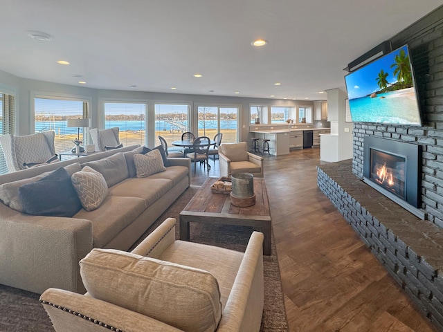 living room featuring recessed lighting, plenty of natural light, dark wood-type flooring, and a brick fireplace