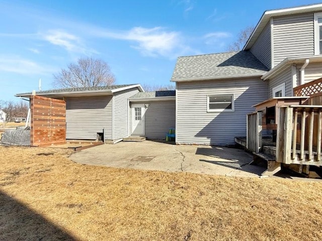 rear view of property with a wooden deck, roof with shingles, and a patio area