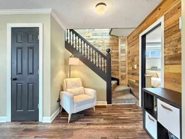 sitting room featuring ornamental molding, a textured ceiling, wood finished floors, wood walls, and stairs