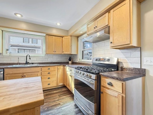 kitchen with under cabinet range hood, stainless steel range with gas stovetop, light brown cabinetry, dark wood-style floors, and a sink