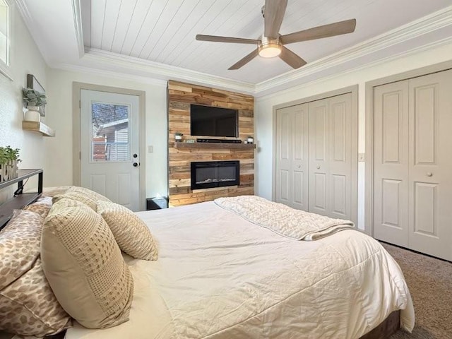 carpeted bedroom with ceiling fan, a large fireplace, two closets, and ornamental molding