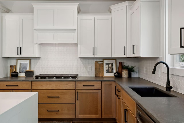 kitchen with stainless steel appliances, backsplash, dark countertops, a sink, and white cabinetry
