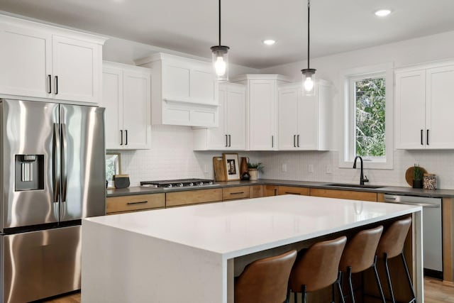 kitchen with stainless steel appliances, a center island, a sink, backsplash, and decorative light fixtures