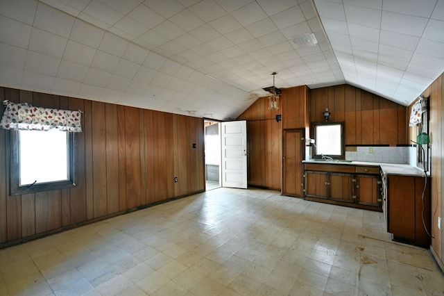 kitchen with wood walls, brown cabinetry, light countertops, lofted ceiling, and light floors