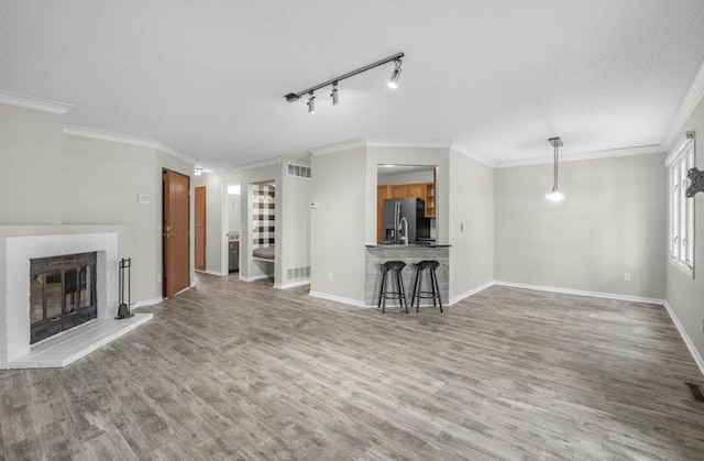 unfurnished living room with visible vents, a brick fireplace, baseboards, wood finished floors, and a textured ceiling