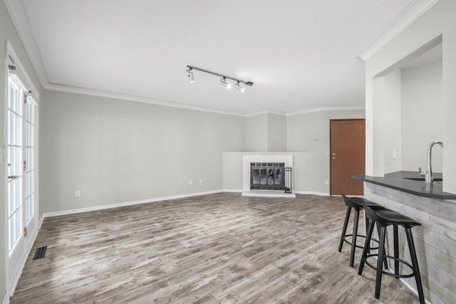 living room with visible vents, ornamental molding, a glass covered fireplace, wood finished floors, and baseboards