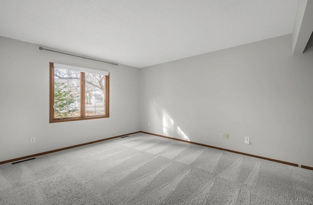 carpeted empty room featuring baseboards, visible vents, and a textured ceiling