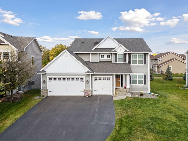 traditional-style house with a front lawn, aphalt driveway, board and batten siding, an attached garage, and a shingled roof