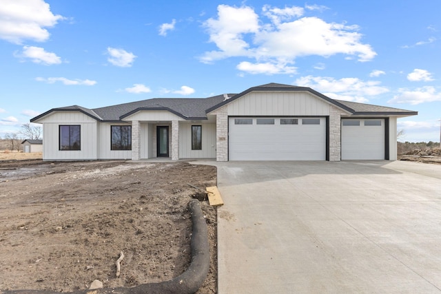 view of front of property with stone siding, an attached garage, concrete driveway, and a shingled roof