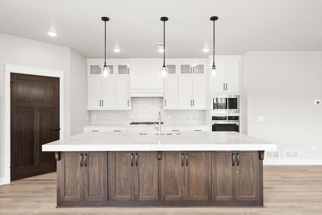 kitchen with visible vents, tasteful backsplash, stainless steel appliances, light wood-style floors, and a large island with sink