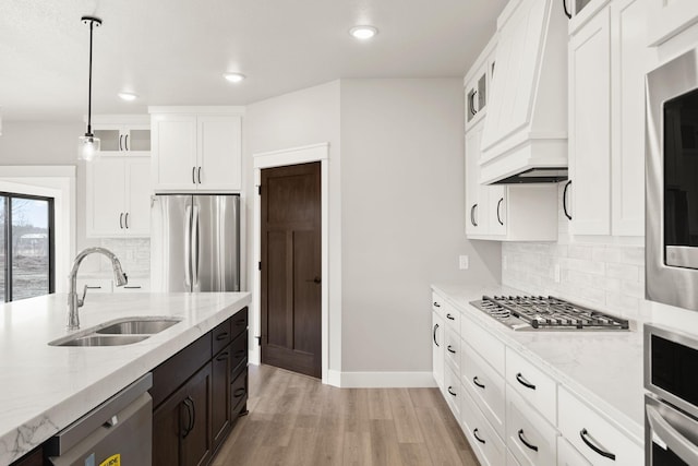 kitchen with a sink, glass insert cabinets, light wood-style floors, appliances with stainless steel finishes, and white cabinetry