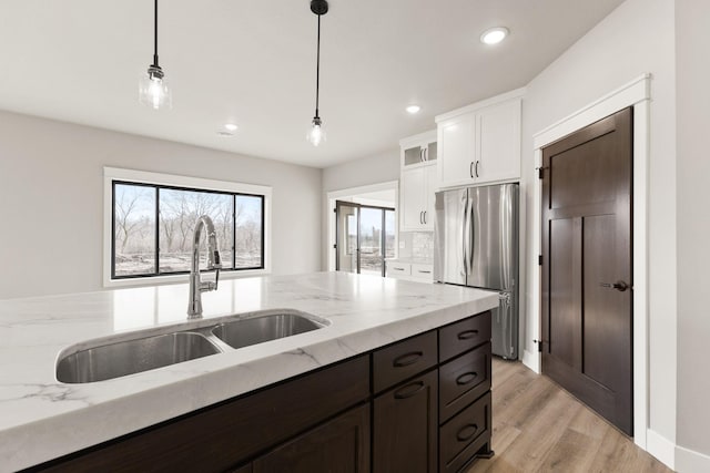 kitchen featuring pendant lighting, light stone counters, freestanding refrigerator, white cabinets, and a sink