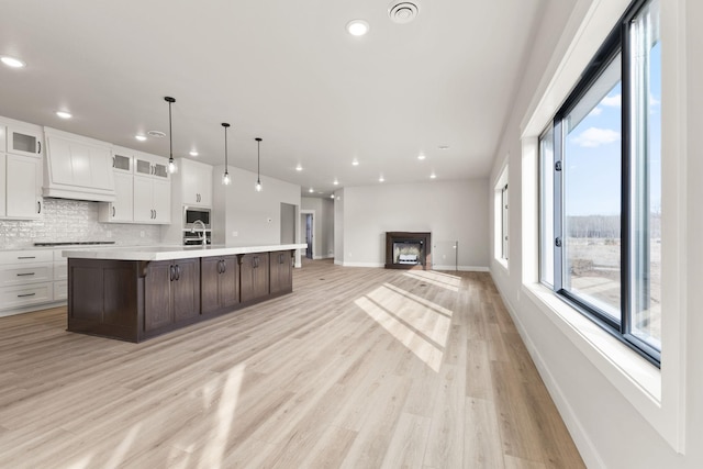 kitchen with light wood finished floors, light countertops, glass insert cabinets, white cabinetry, and backsplash