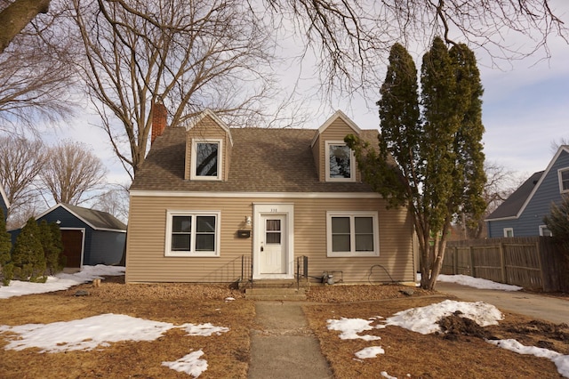 new england style home with an outbuilding, a chimney, roof with shingles, and fence