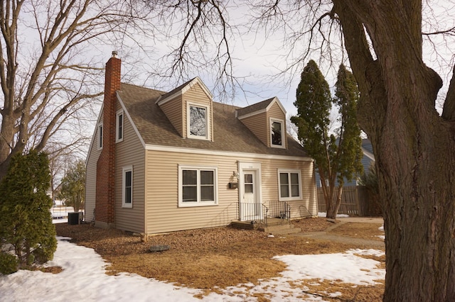 cape cod home featuring central air condition unit, a chimney, roof with shingles, and fence