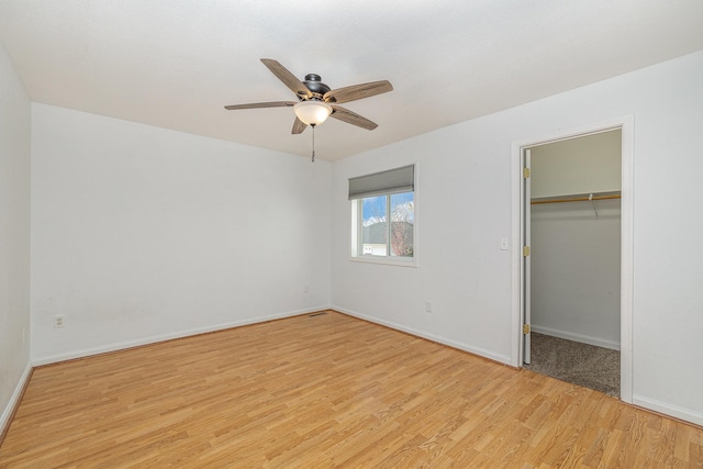 unfurnished bedroom featuring baseboards, ceiling fan, a spacious closet, and light wood finished floors