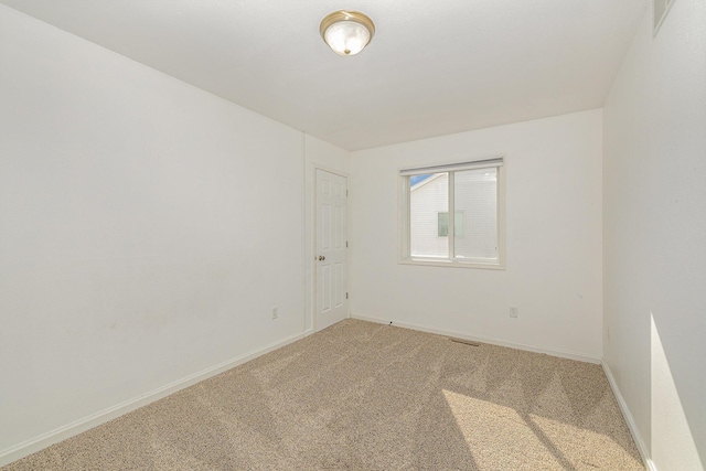 spare room featuring light colored carpet and baseboards