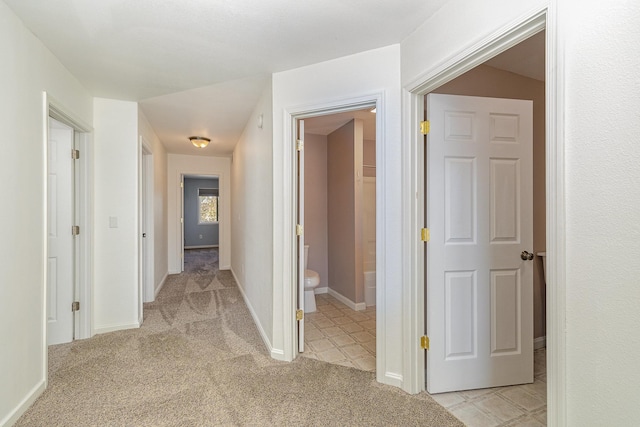 hallway featuring baseboards and light carpet