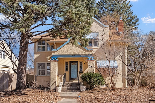 view of front of home featuring stucco siding, a chimney, and fence