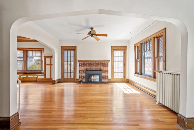 unfurnished living room with a brick fireplace, light wood-style flooring, radiator heating unit, and crown molding