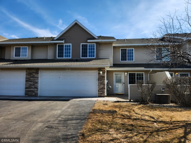 multi unit property featuring central AC unit, stone siding, and driveway