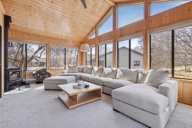 carpeted living area featuring high vaulted ceiling, wooden walls, a healthy amount of sunlight, and a wood stove