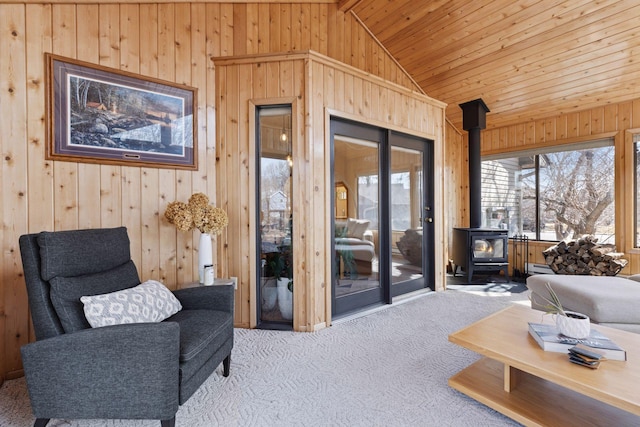 carpeted living room featuring wooden walls, lofted ceiling, baseboard heating, wooden ceiling, and a wood stove