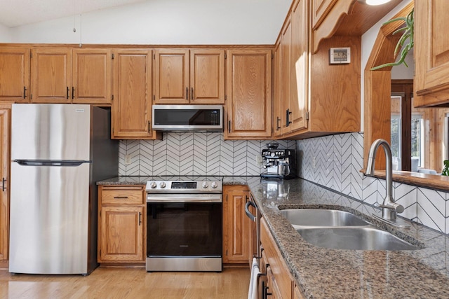 kitchen with lofted ceiling, dark stone countertops, light wood-style flooring, stainless steel appliances, and a sink